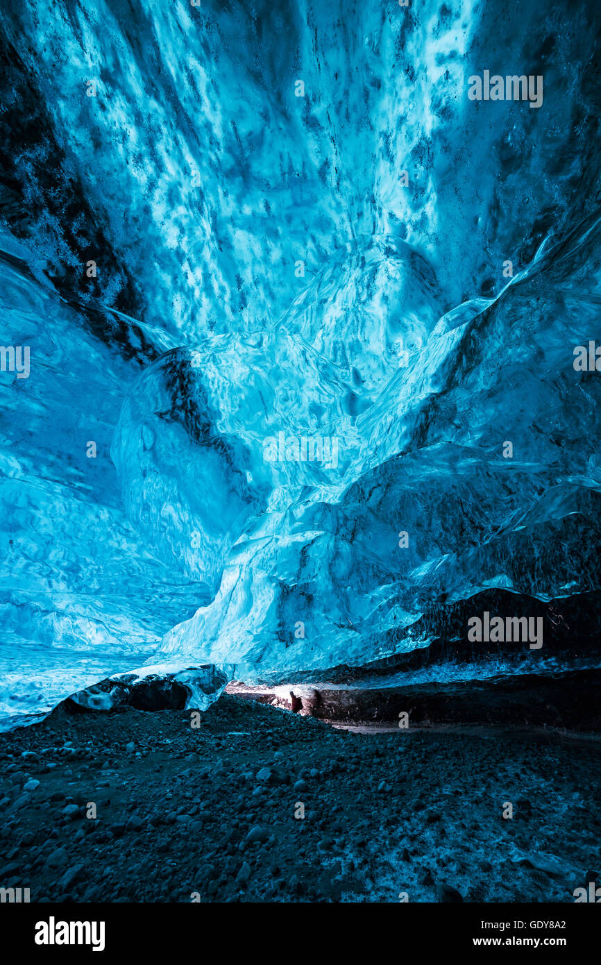 Man inside an immense ice cave, very small in comparison to the size of the surroundings, Ice is glowing blue with almost magica Stock Photo