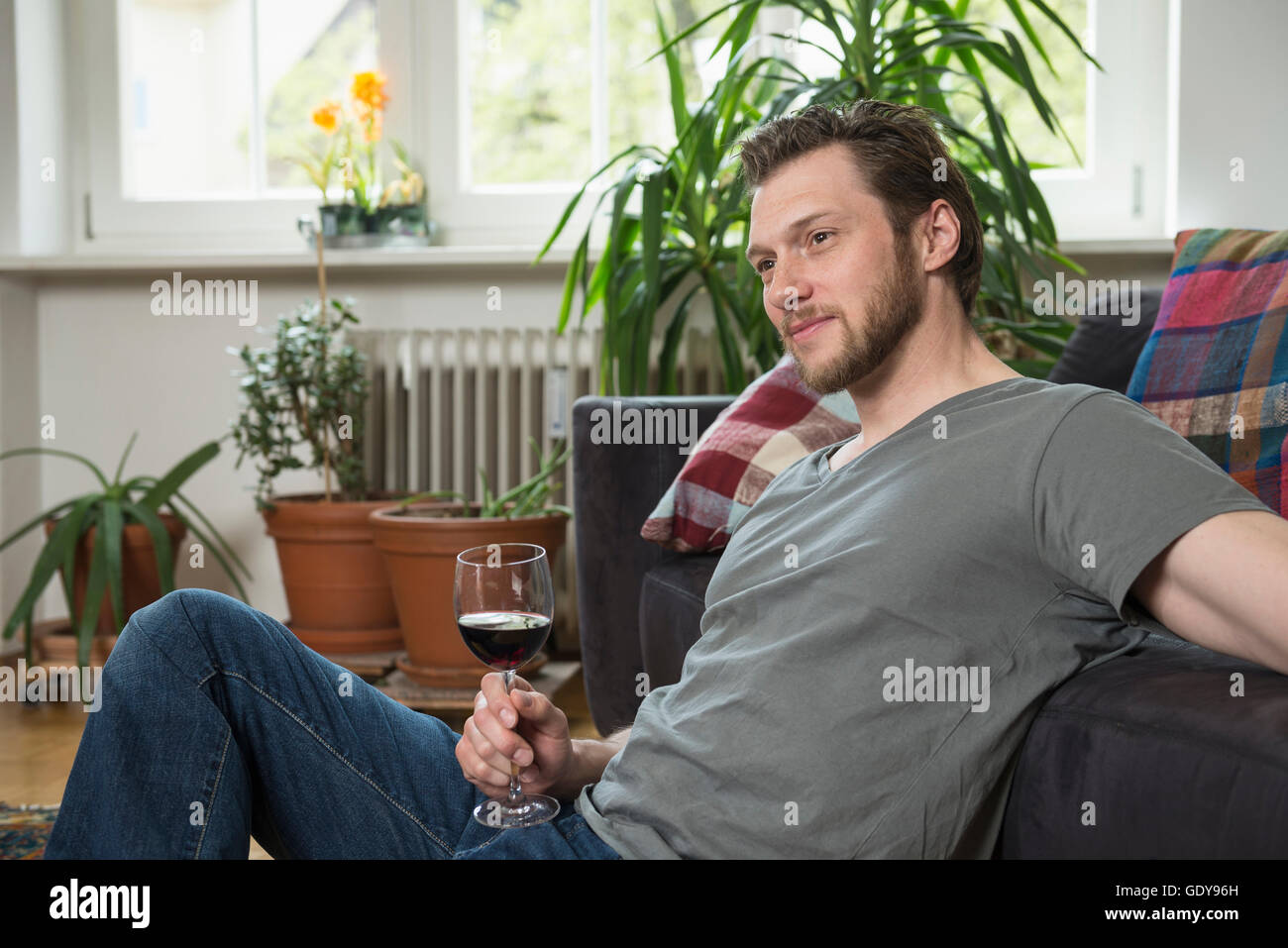 Thoughful mid adult man drinking red wine in living room, Munich, Bavaria, Germany Stock Photo