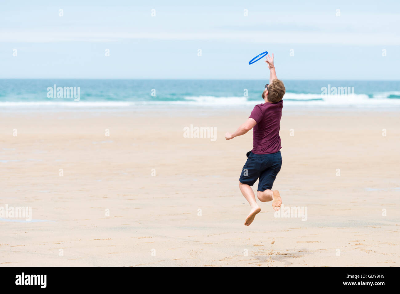A young man playing a bat and ball game on a beach wearing casula clothes in summer UK Stock Photo