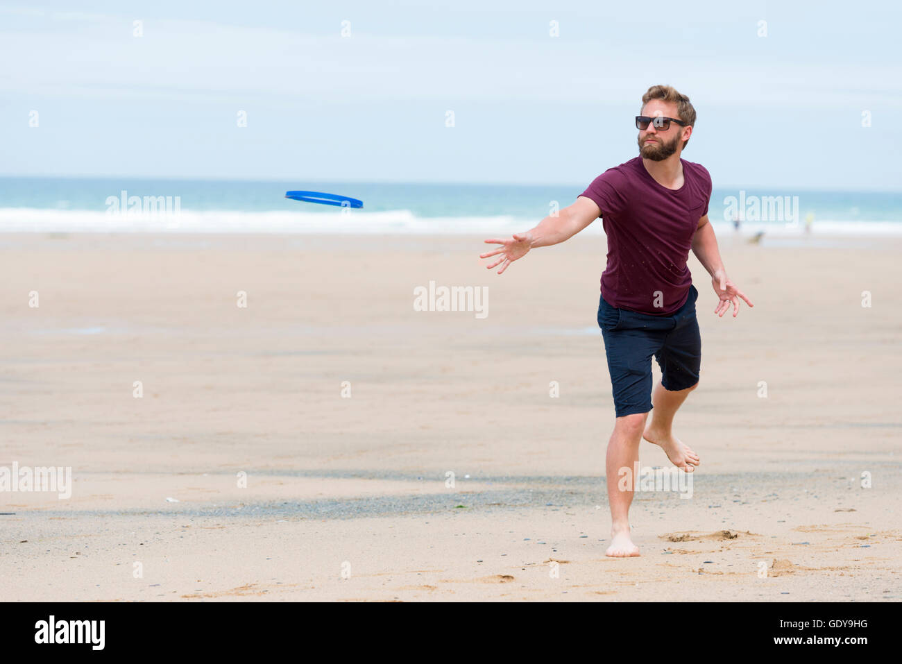 A young man playing a bat and ball game on a beach wearing casula clothes in summer UK Stock Photo