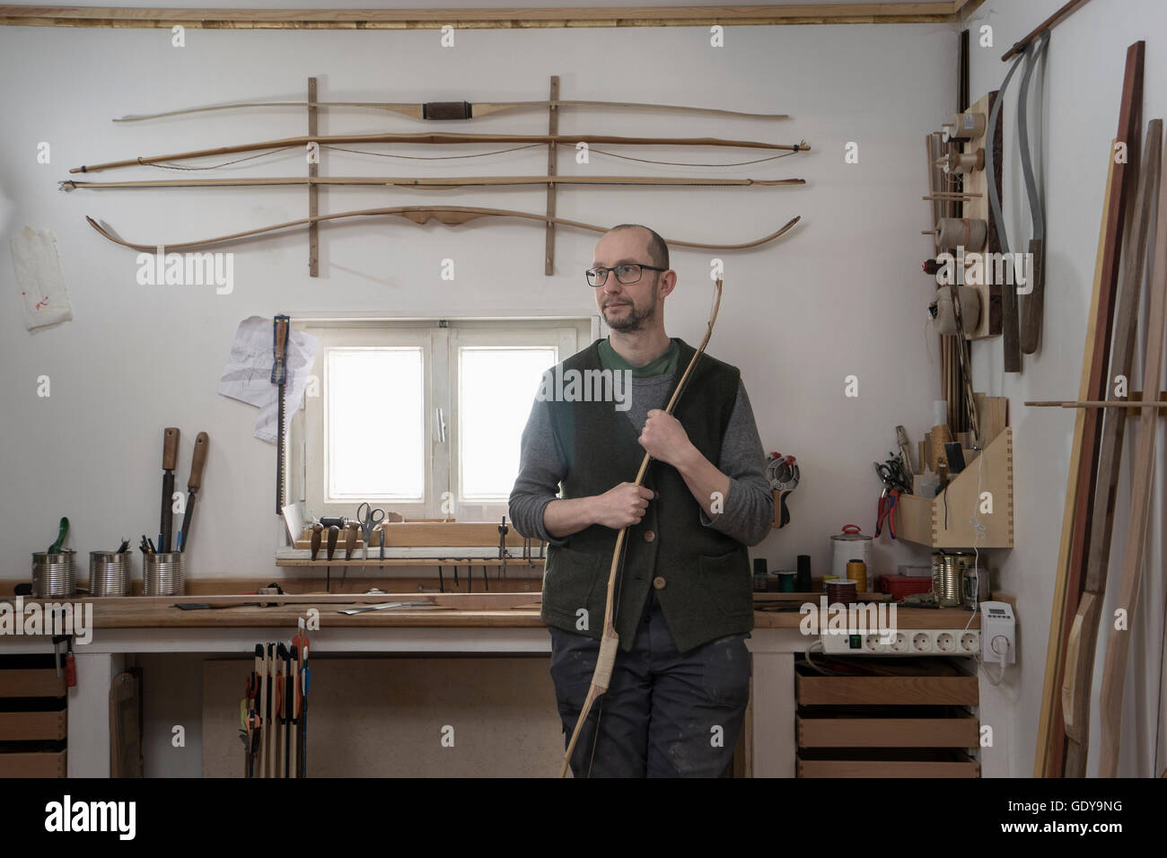 Male bow maker holding bow and thinking in workshop, Bavaria, Germany Stock Photo