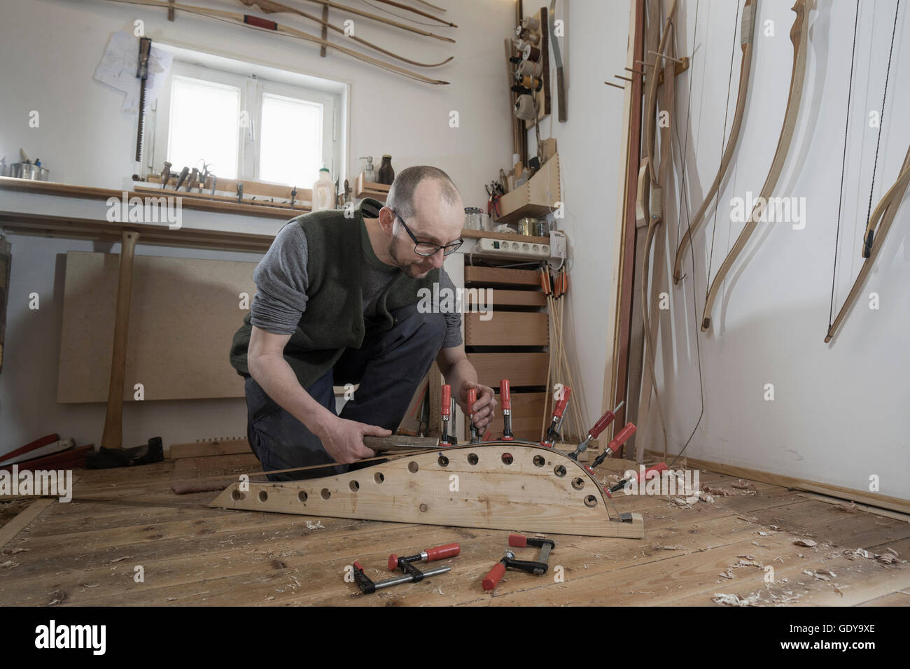Male bow maker fixing wood in bow shape in workshop, Bavaria, Germany Stock Photo