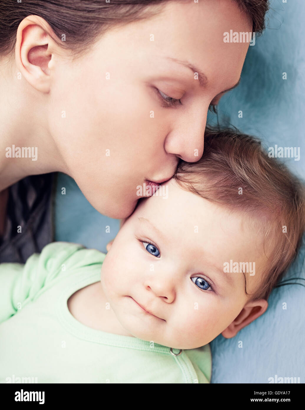 Baby boy with beautiful blue eyes being kissed by his mother. Stock Photo