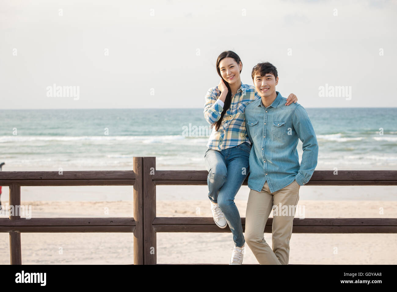 Young smiling couple posing at rail against beach Stock Photo