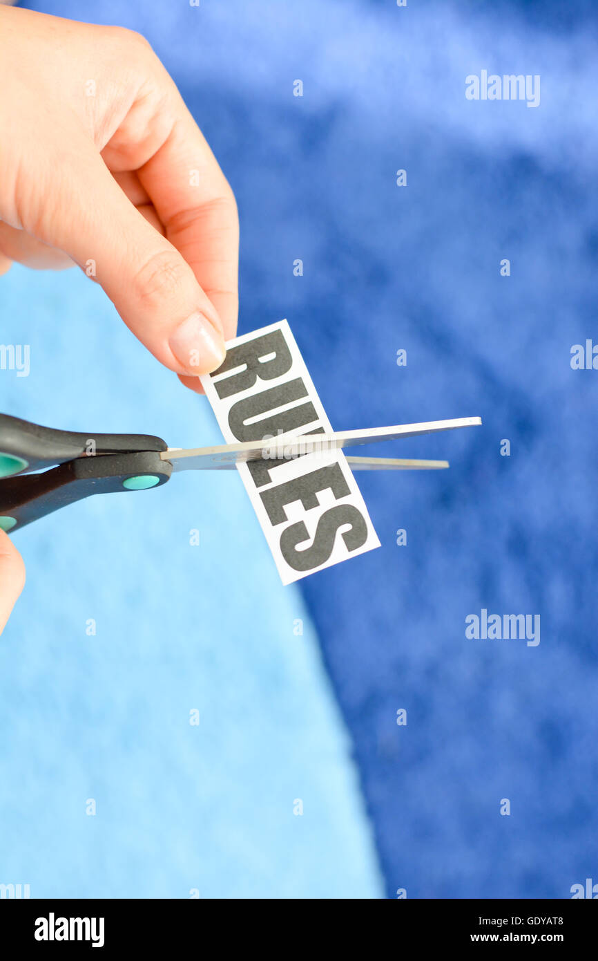 Woman hands cutting with scissors a printout reading 'RULES' Stock Photo