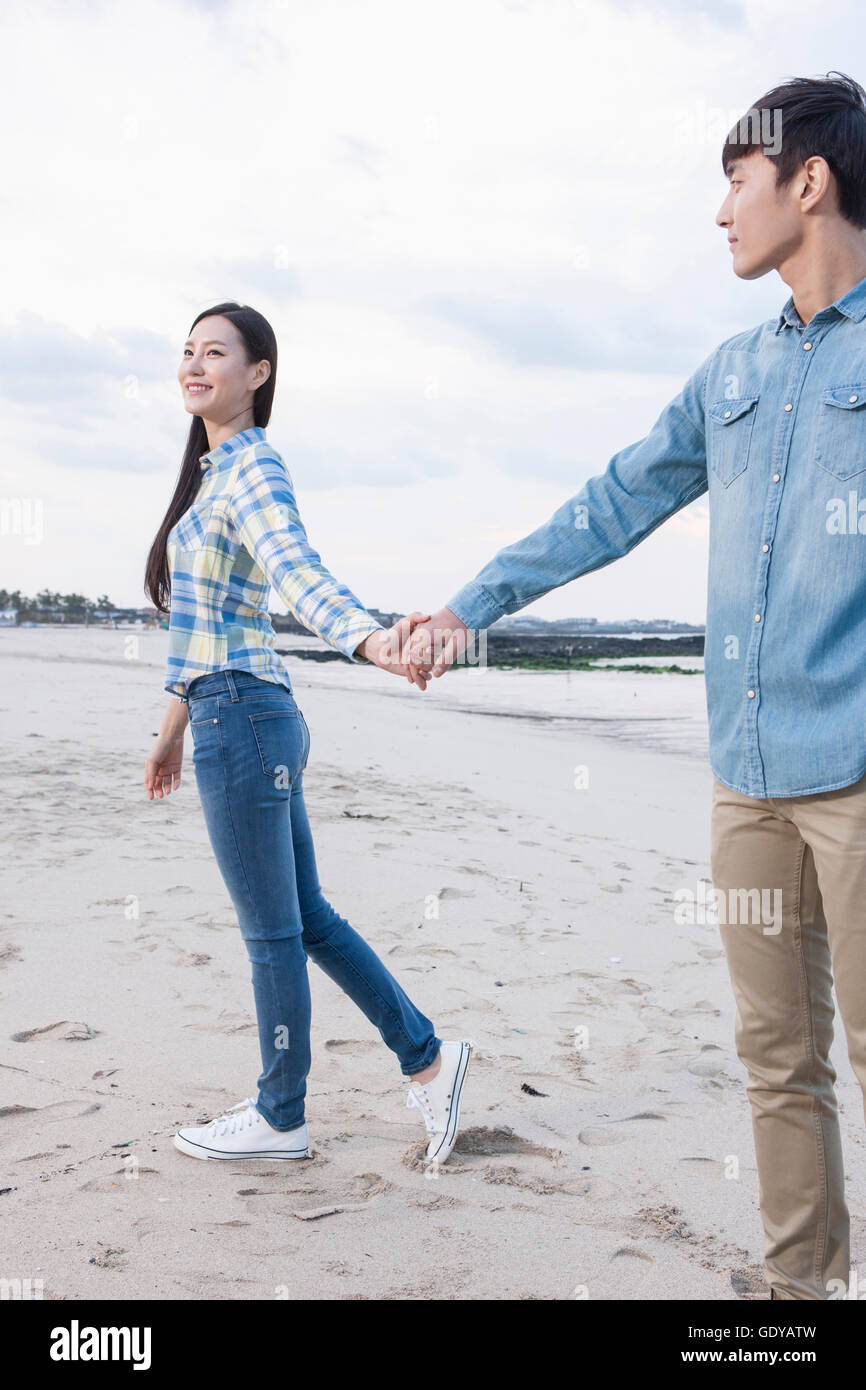 Side view of young smiling couple walking hand in hand on beach Stock ...