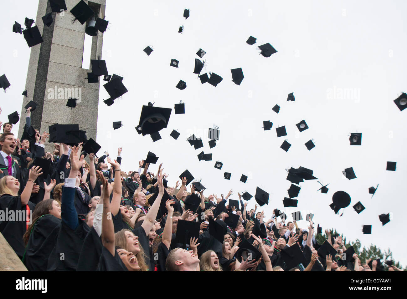 Higher Education in the UK: Aberystwyth university students wearing traditional gowns, capes and mortar boards throwing their caps in the air in the traditional celebration manner at their graduation day ceremony, July 2016 Stock Photo