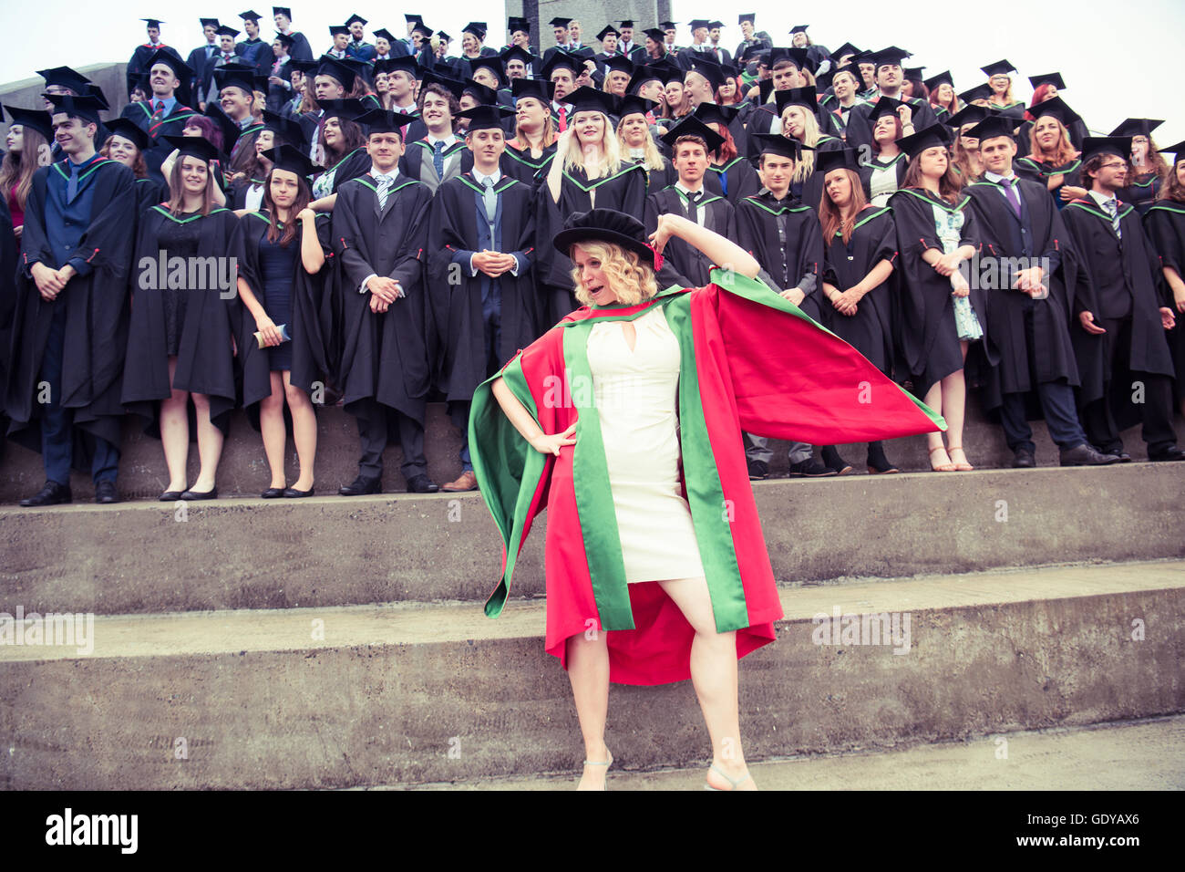 Higher Education in the UK:  A successful woman PhD (Doctoral) degree graduate standing and posing in front of a group Aberystwyth university students wearing traditional gowns, capes and mortar boards at their graduation day ceremony, July  2016 Stock Photo