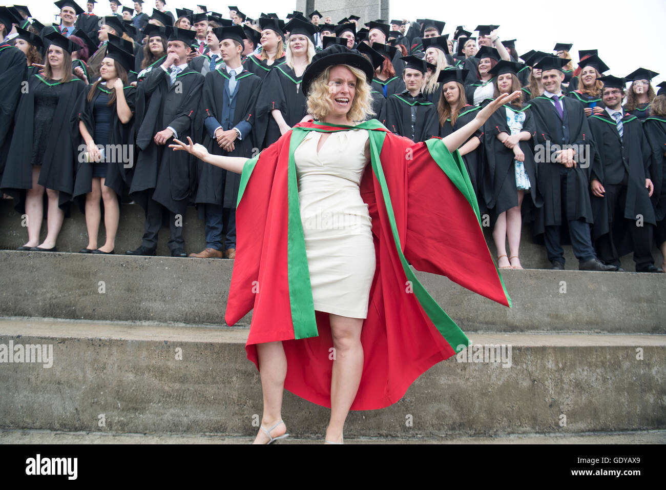 Higher Education in the UK: A successful woman PhD (Doctoral) degree  graduate standing and posing in front of a group Aberystwyth university  students wearing traditional gowns, capes and mortar boards at their