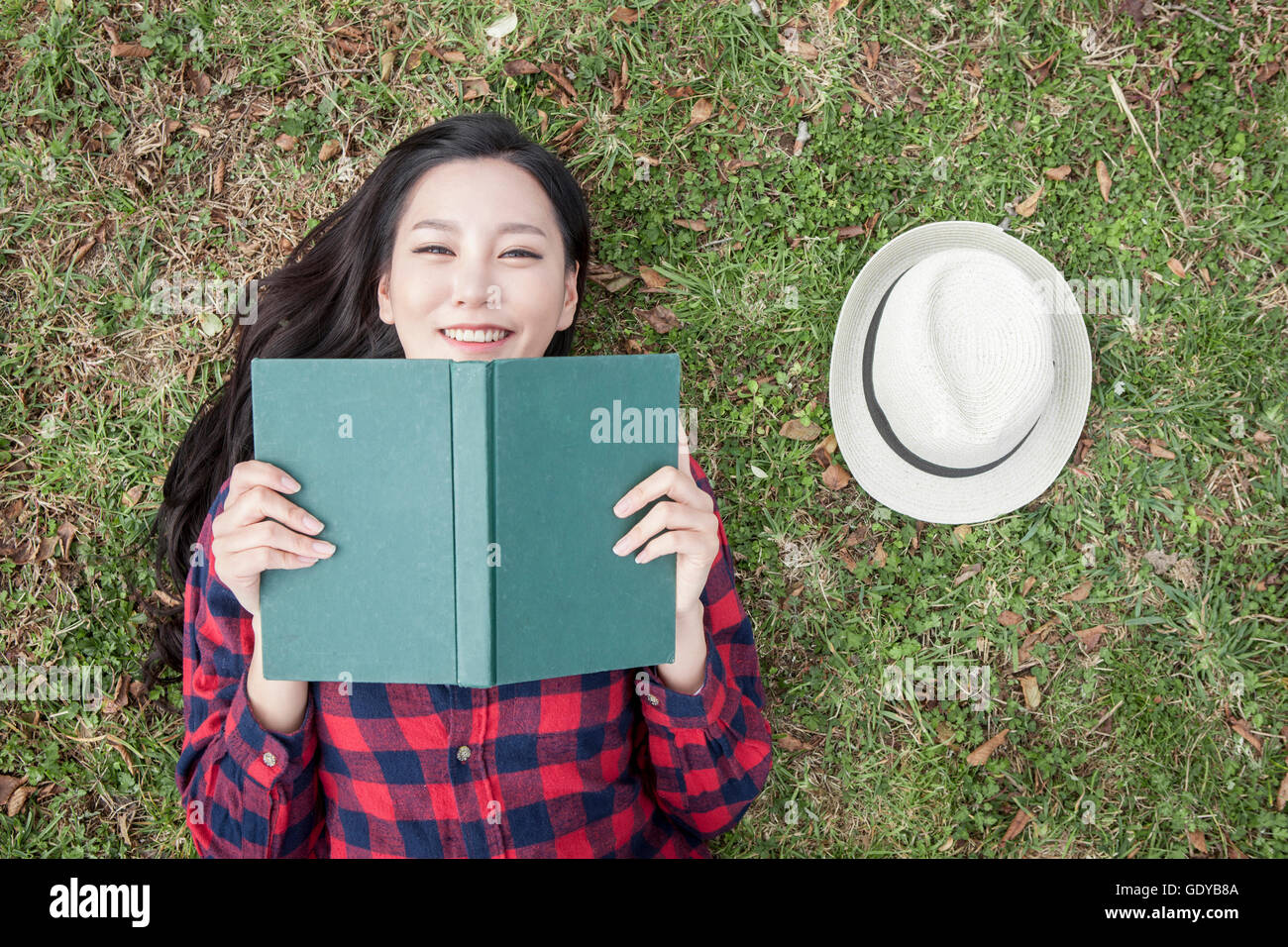 Portrait nof young smiling woman with a book lying down on grassland ...