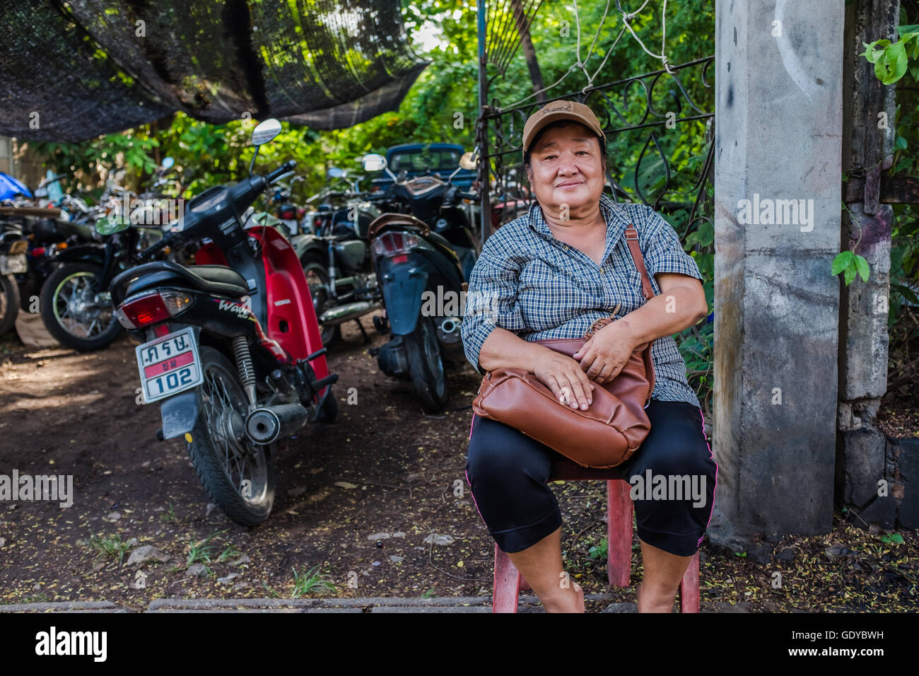 Thai lady sitting in chair by bike mechanics waiting for scooter to be repaired,Chiang Mai,Thailand Stock Photo