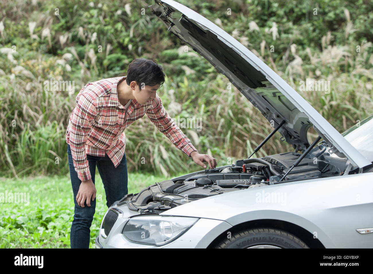 Side view of young man standing and repairing his broken car Stock Photo