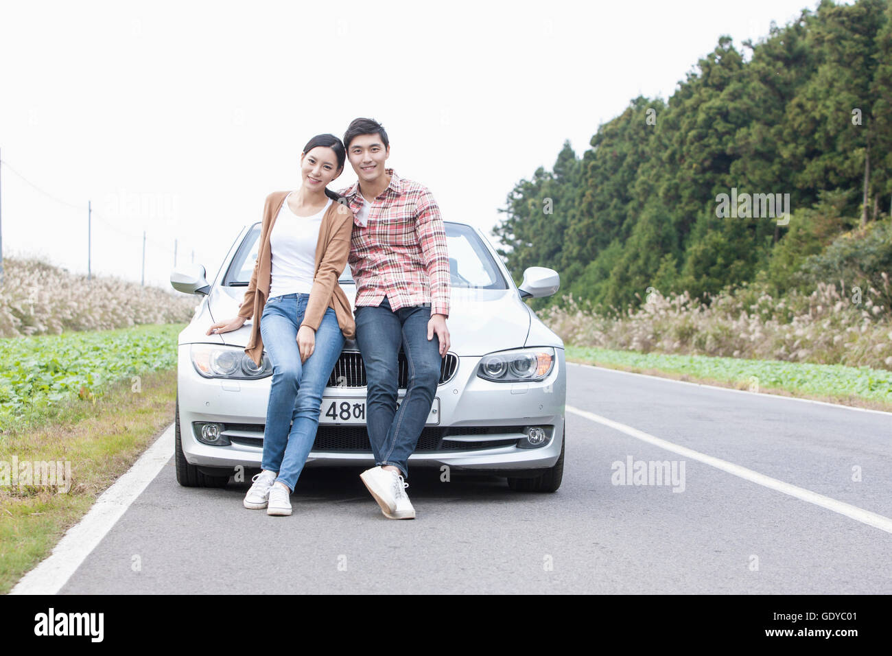 Young smiling couple sitting on a car Stock Photo - Alamy