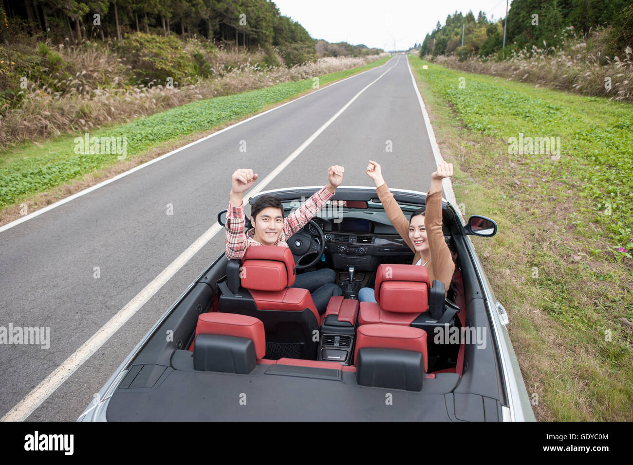 Young smiling couple in a car raising their arms Stock Photo