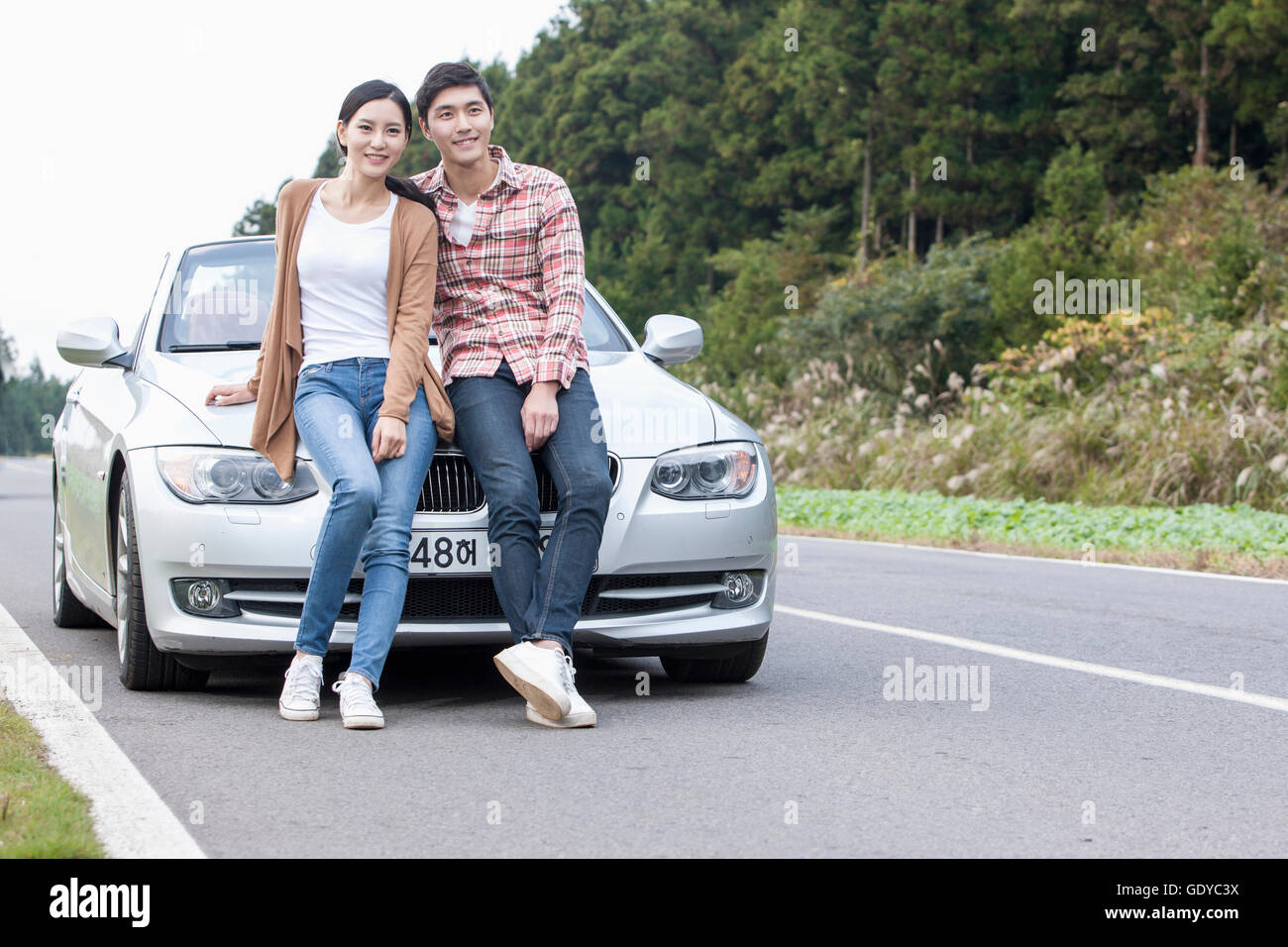 Young smiling couple sitting on a car on a road Stock Photo - Alamy