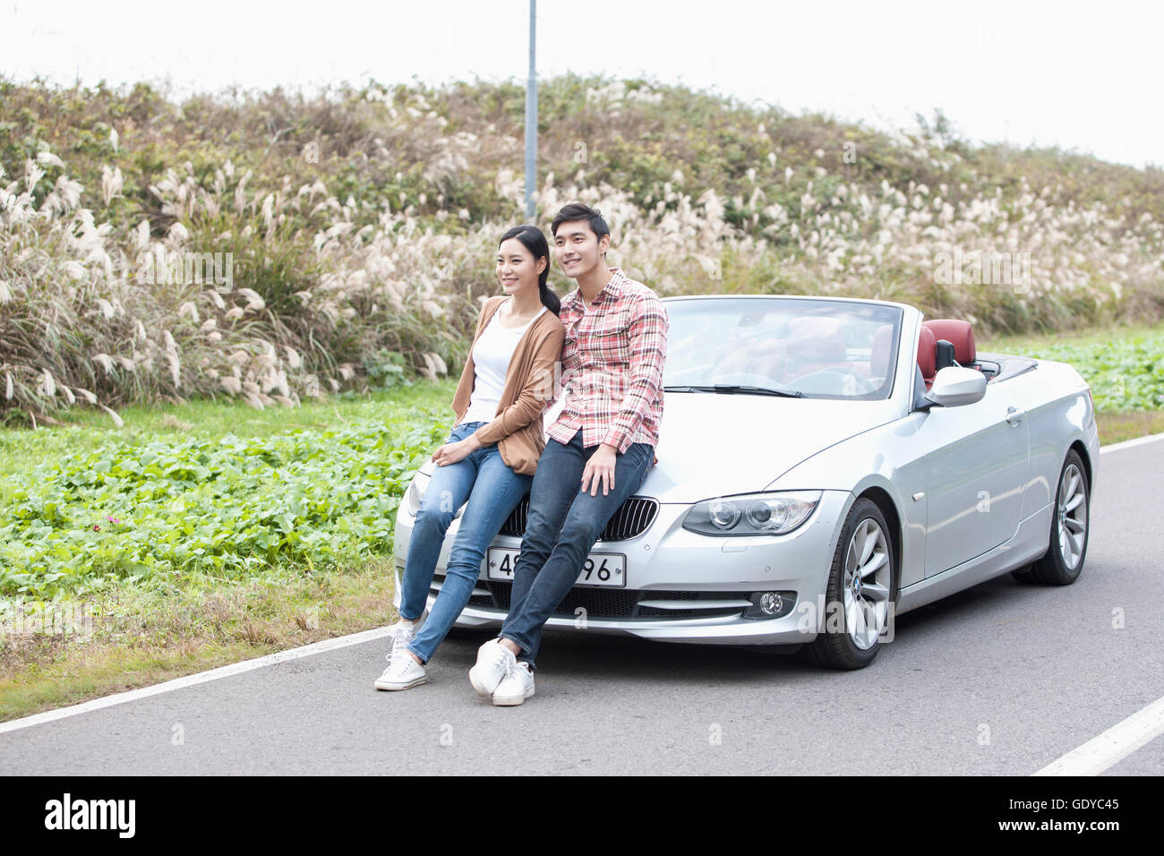 Young smiling couple sitting on a car on a road Stock Photo - Alamy