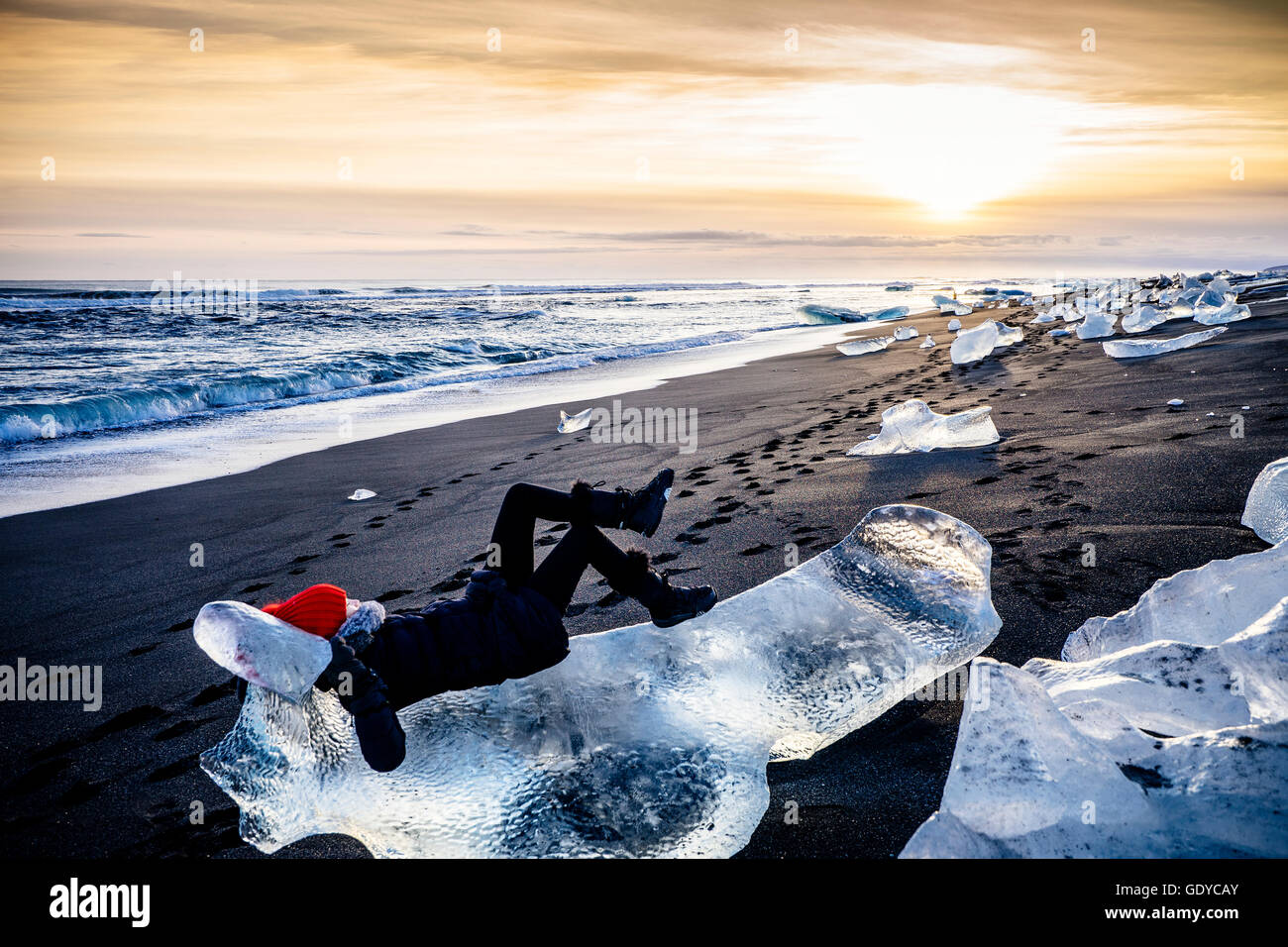 Woman laying on large ice chunk on beach at sunset, Iceland Stock Photo