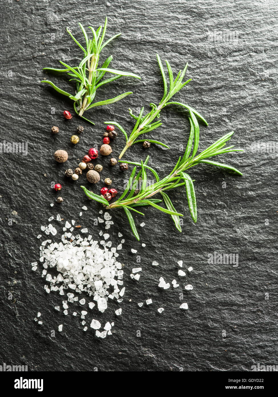 Salt, rosemary and peppercorns on the graphite board. Stock Photo