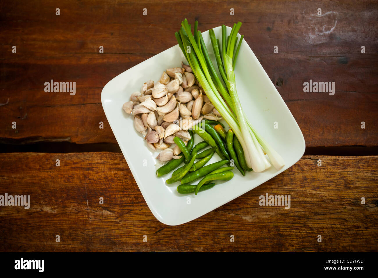 Fresh spring onion, bird eye green chilli and baby garlic on plate. Set of traditional thai spices. Stock Photo
