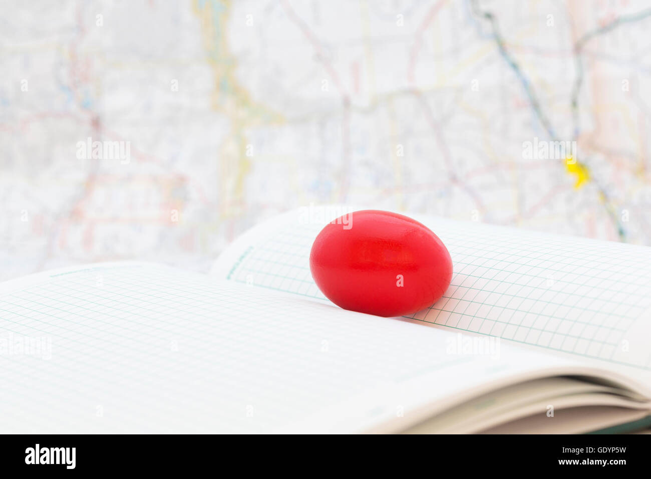 Red egg on ledger pages with map behind shows troubled financial and business times.  Selective focus on key, nest egg symbol. Stock Photo