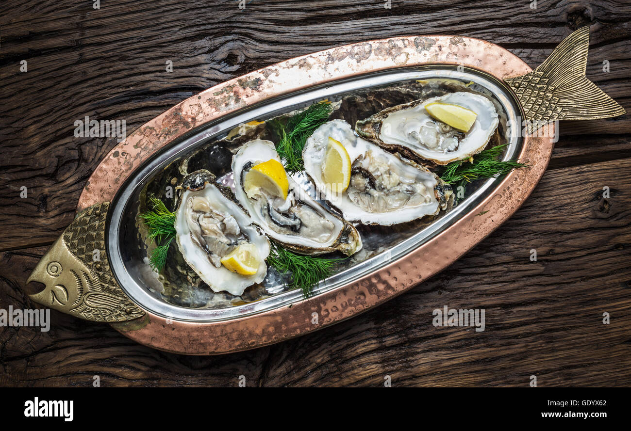 Opened oysters with piece of lemon on the cooper tray. Stock Photo