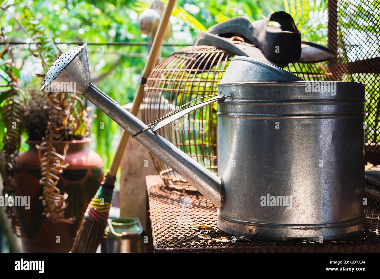 Watering can on rusty table, bird cage background Stock Photo