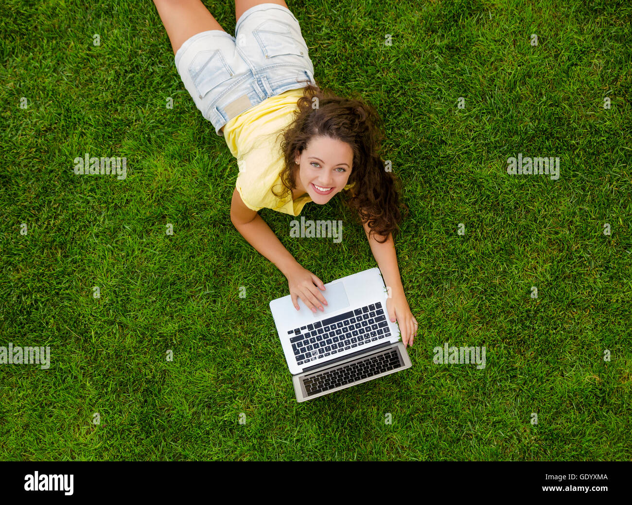 Beautiful young woman lying on the grass and working with a laptop ...