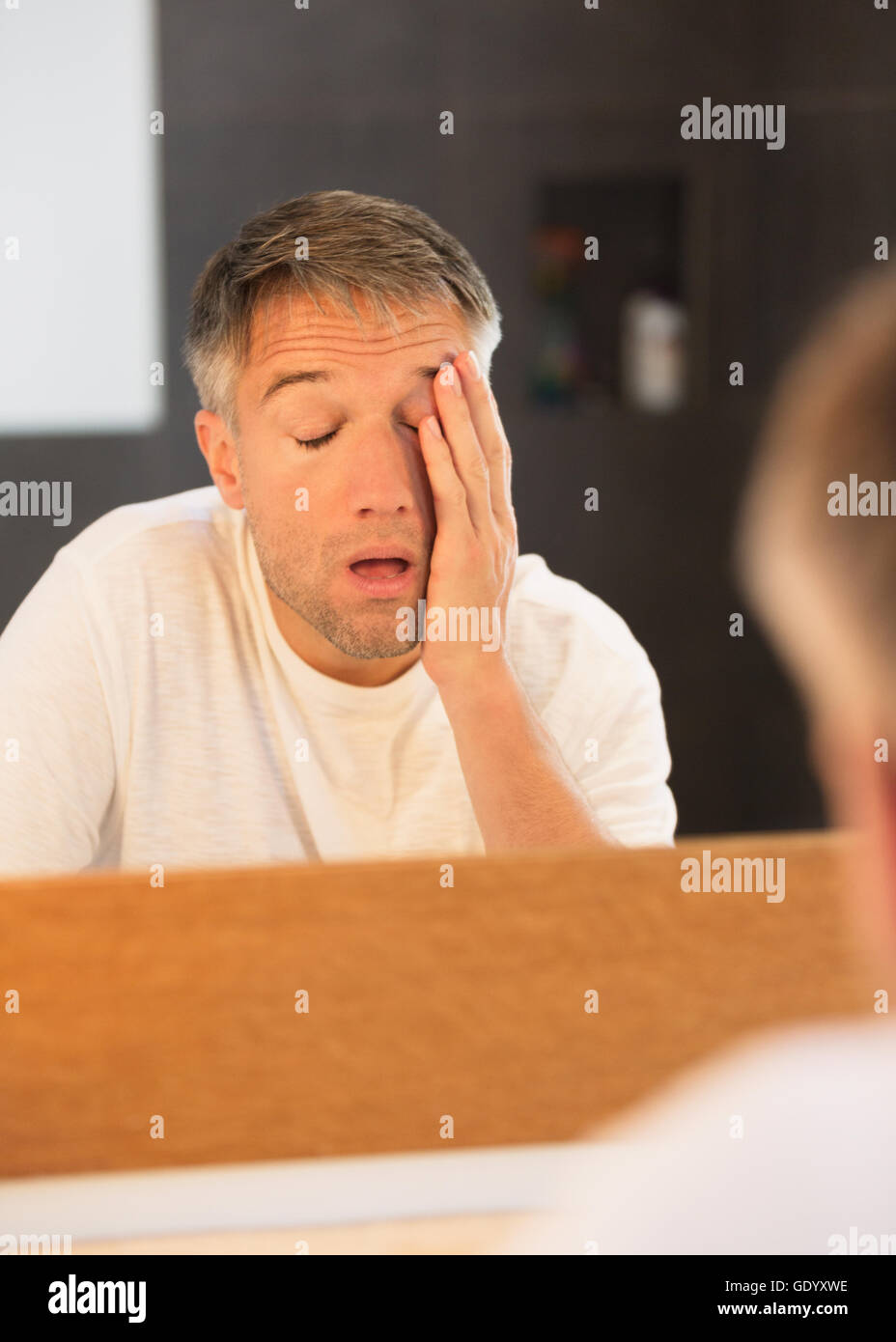 Tired man with head in hands at bathroom mirror Stock Photo