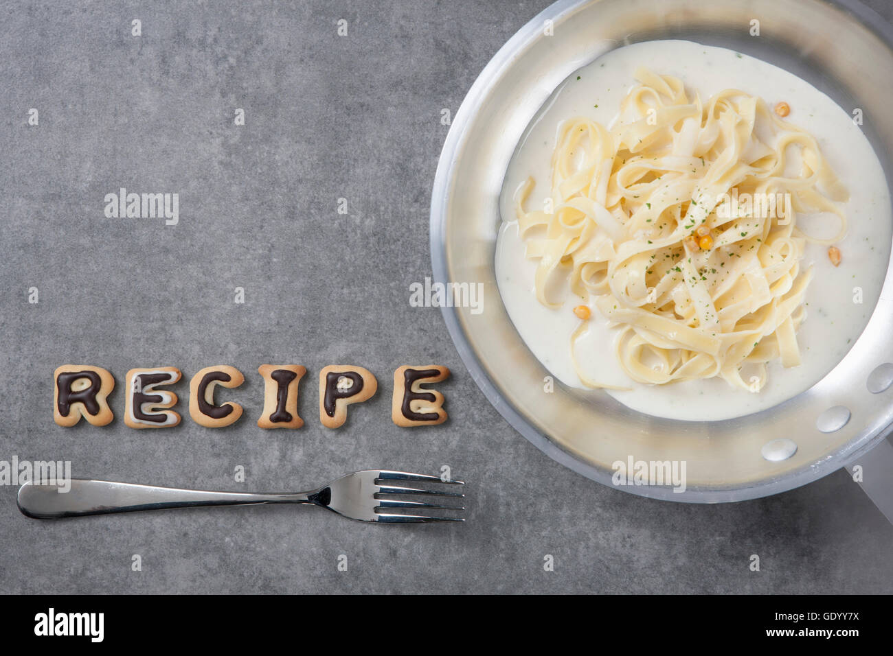 Typographical word of RECIPE made of alphabet cookies with fork and bowl of noodles Stock Photo