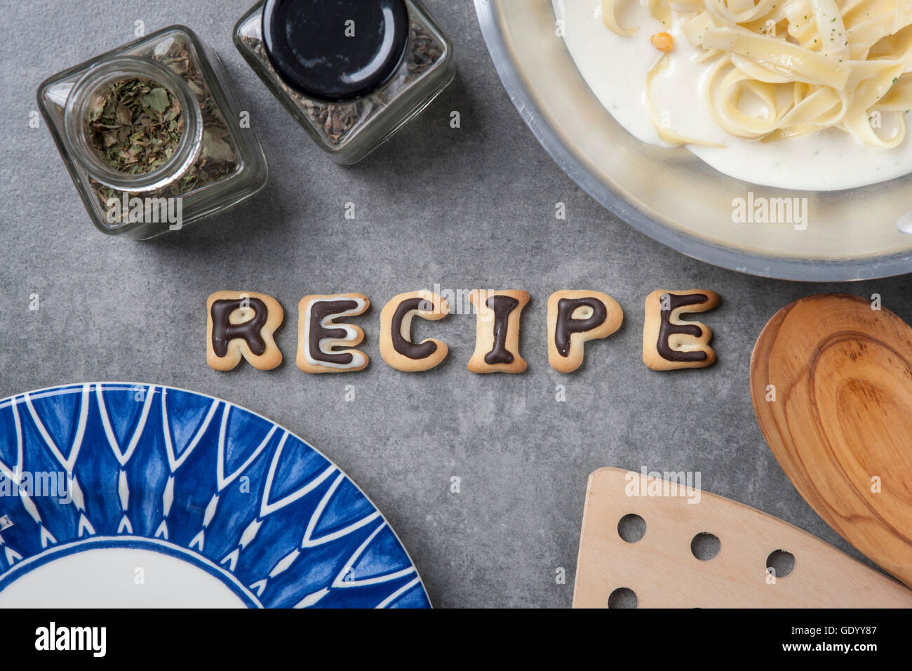 Typographical word of RECIPE made of alphabet cookies with herbs, noodles and plates Stock Photo