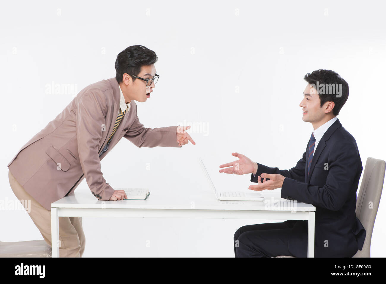 Side v of two business men at table face to face, one surprised and the other smiling Stock Photo