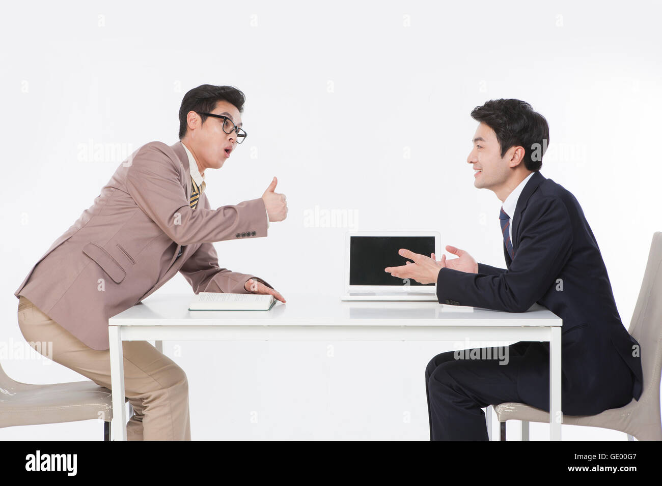 Side view of two business men at table face to face, one surprised and the other smiling Stock Photo