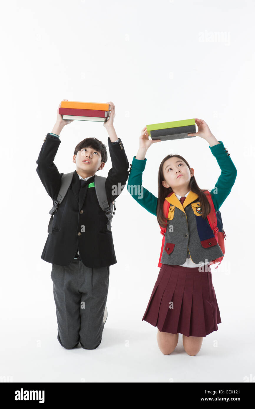 School boy and school girl sitting on their knees holding up books and looking up Stock Photo