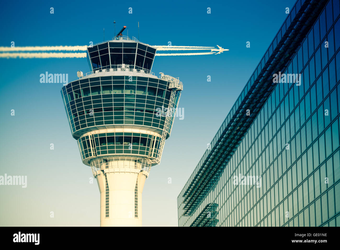Flights management air control tower and passenger terminal in Munich international airport with flying plane in clear sky Stock Photo