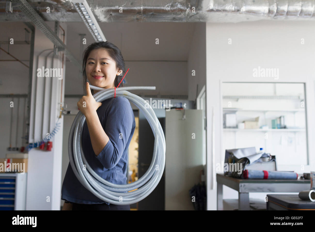 Young female engineer with pipe on her shoulder in an industrial plant, Freiburg im Breisgau, Baden-Württemberg, Germany Stock Photo