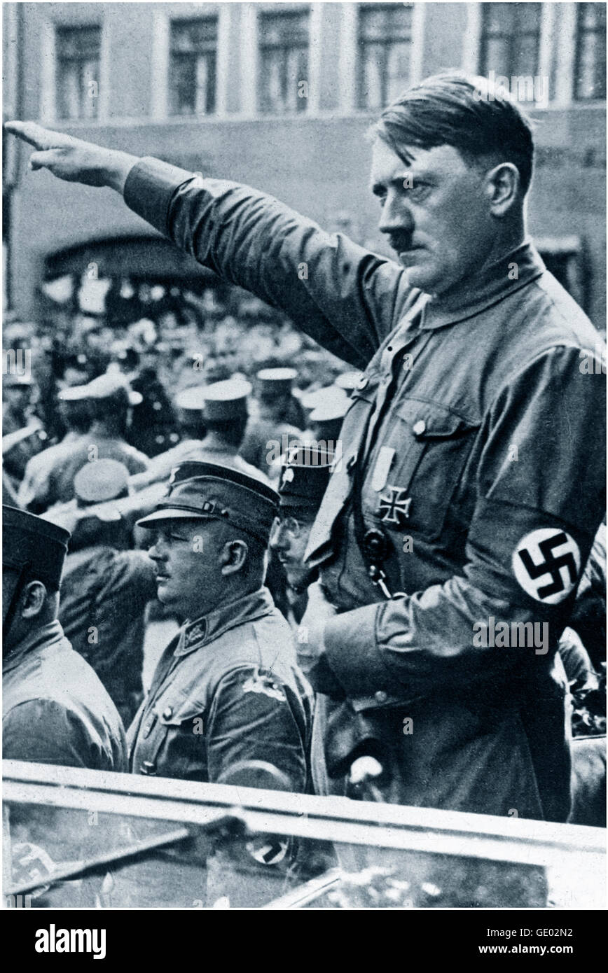 Adolf Hitler in open car wearing Sturmabteilung uniform and swastika armband performing Nazi salute at a political rally parade in Germany 1930's.  The Sturmabteilung SA; literally 'Storm Detachment') was the Nazi Party's (National Socialist German Workers' Party) original paramilitary wing. It played a significant role in Adolf Hitler's rise to power in the 1920s and 1930s. Its primary purposes were providing protection for Nazi rallies and assemblies, disrupting the meetings of opposing parties. Stock Photo