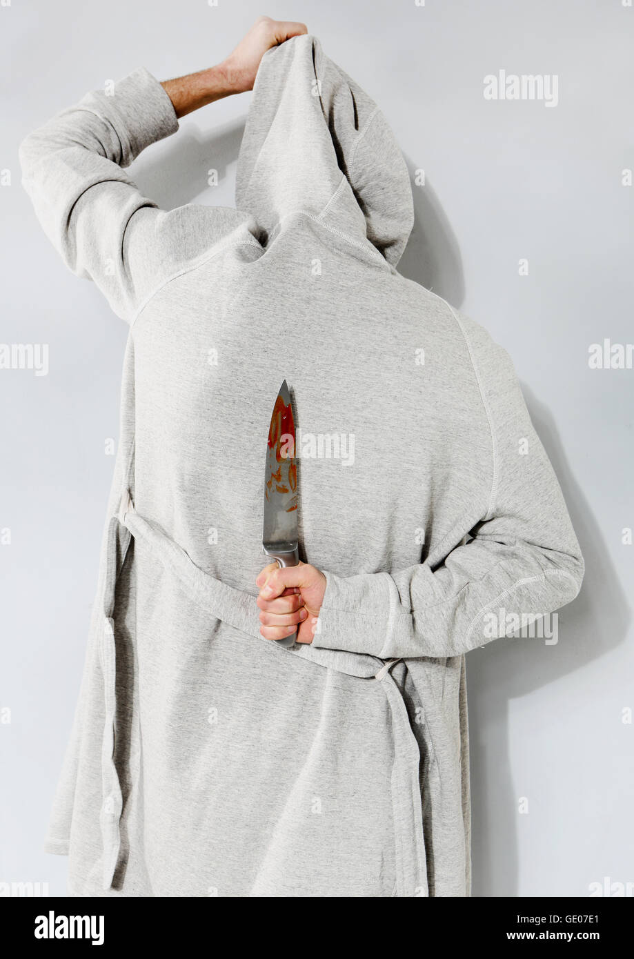 Man with a bloody knife on a gray background. Stock Photo