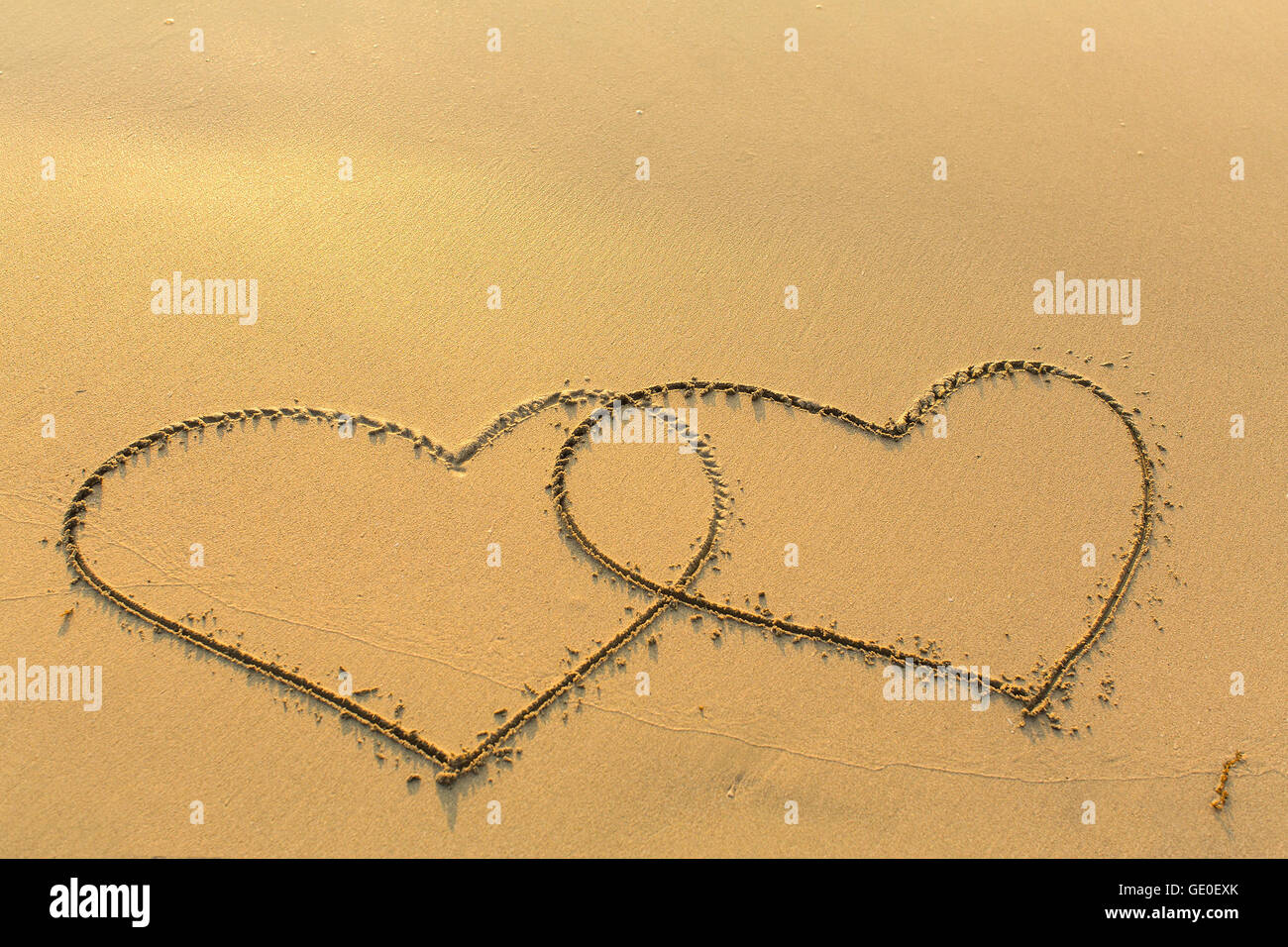 Two lovers hearts drawn on the sand to the sea. Stock Photo