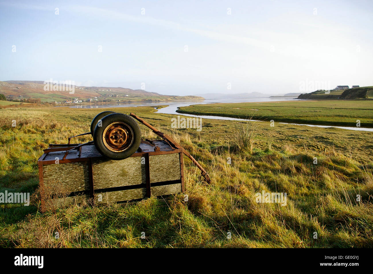 Green field and meandering river in Donegal, Ireland, with an overturned cart or trailer in the foreground Stock Photo