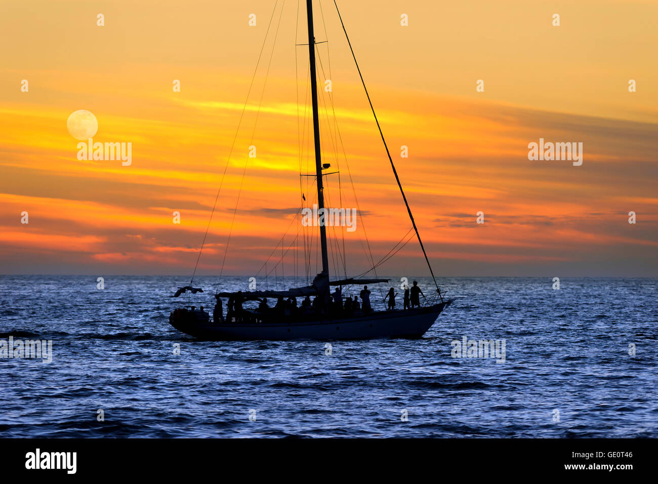 A sailboat full of people saiiing and having fun at sunset on the ocean. Stock Photo