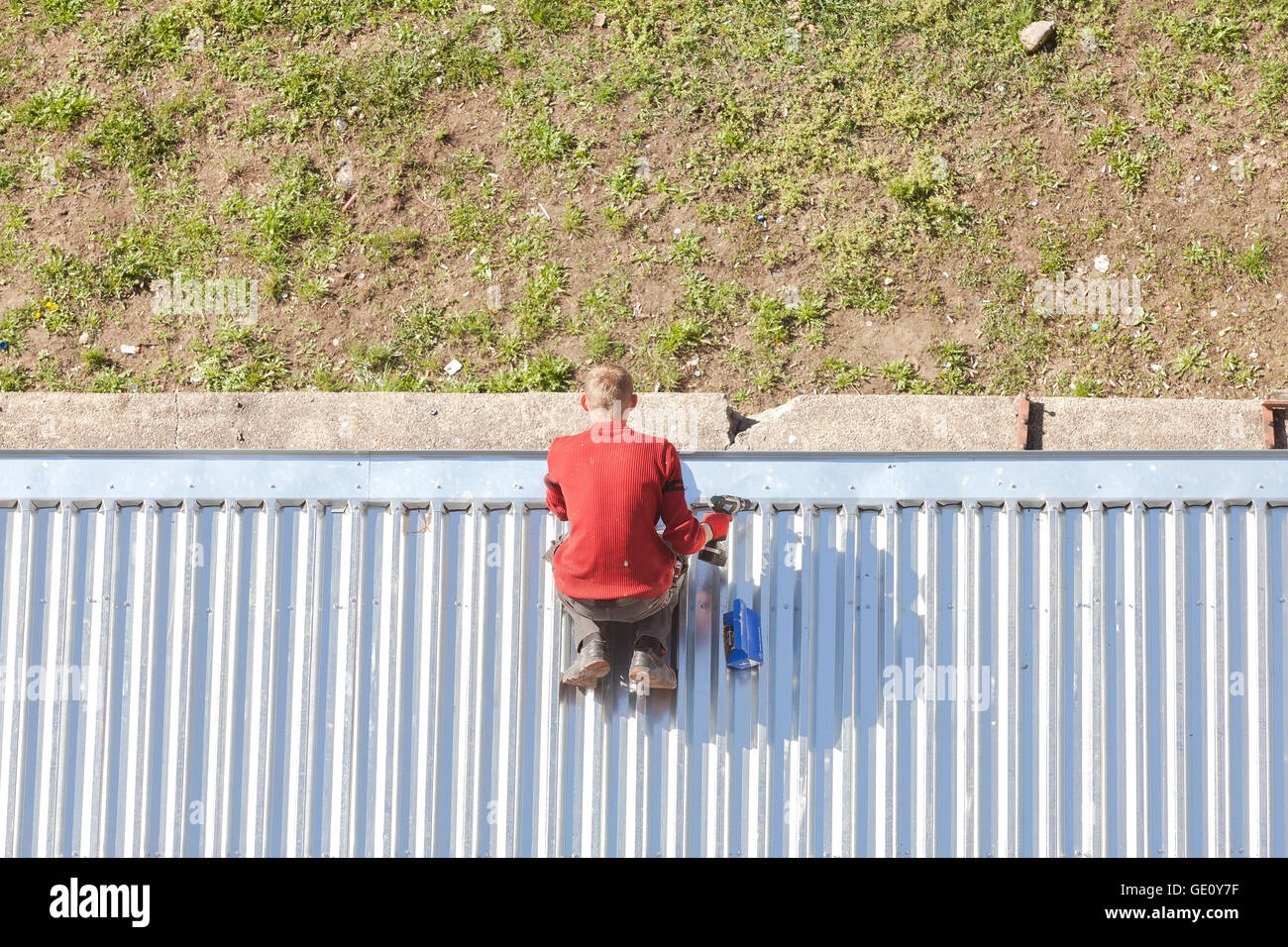 Man with a drill reparing a store roof made of corrugated metal sheets. Stock Photo
