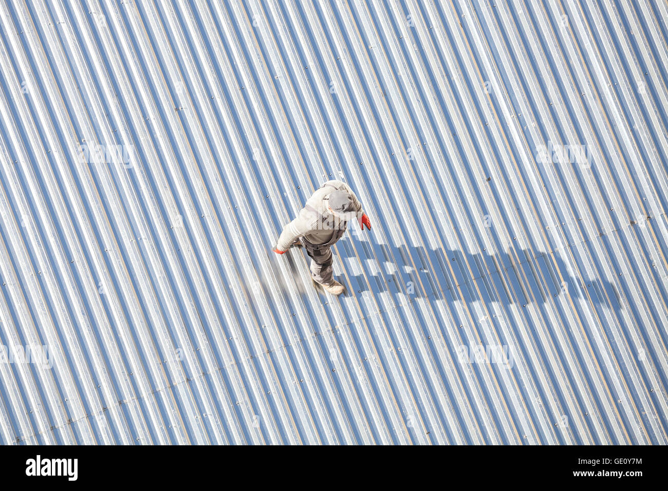 Man inspecting a store roof made of corrugated metal sheets after repair, picture taken from above. Stock Photo