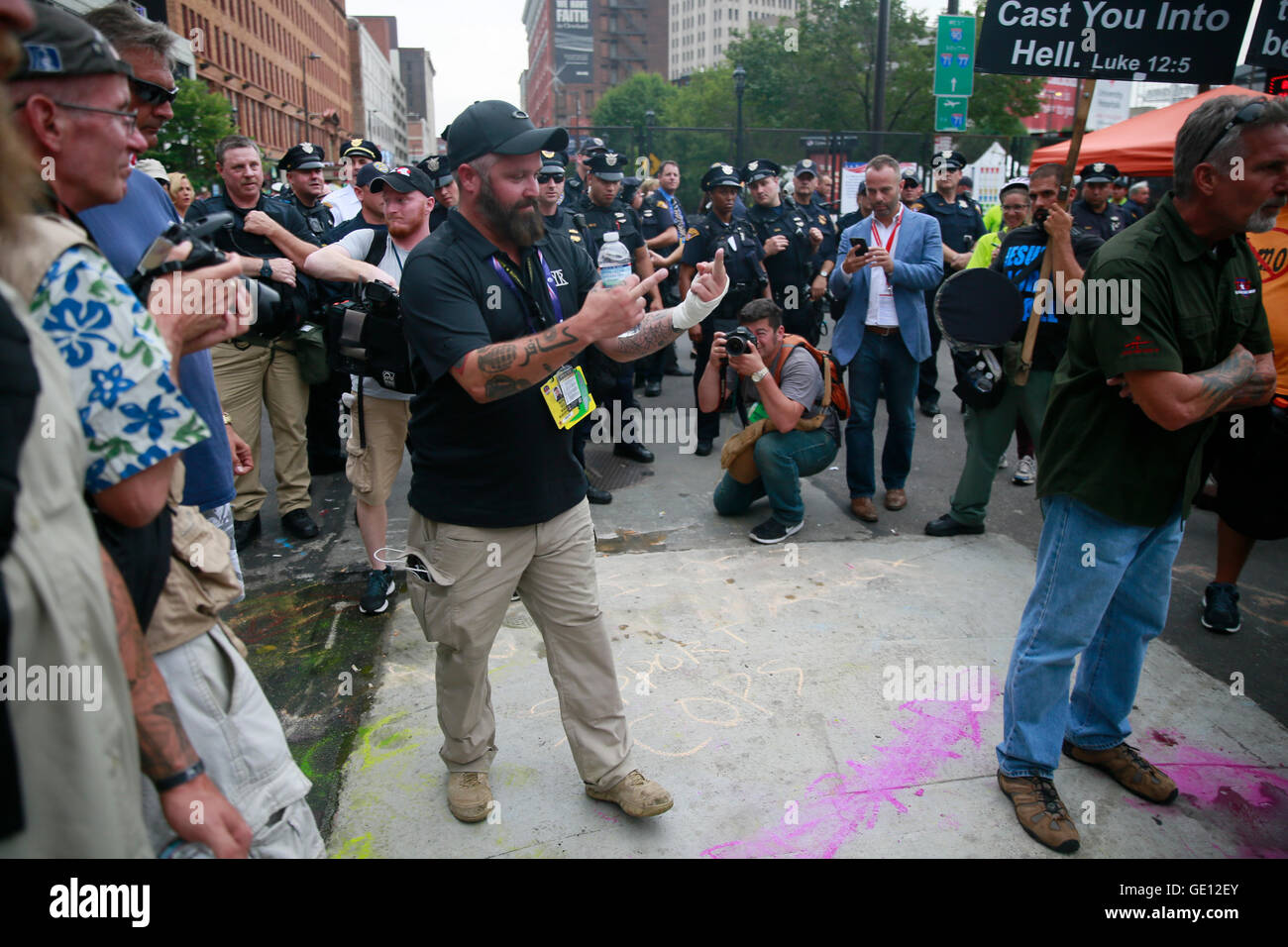 07212016 - Cleveland, Ohio, USA:  A man claiming to be a war veteran, and a patriot flips off anti-police protesters after he poured water on their messages to censor them at the entrance to Quicken Loans Arena on the final day of the 2016 Republican National Convention in downtown Cleveland. The protesters had written, 'Disarm the Police.' Another one of the veterans threatened physical violence, and arrest against the protesters. (Jeremy Hogan) Stock Photo
