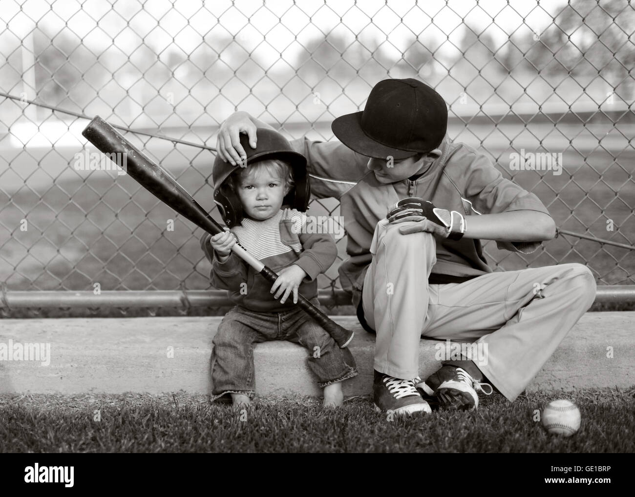 Two boys sitting in baseball park with one Boy wearing his brother's baseball hat Stock Photo