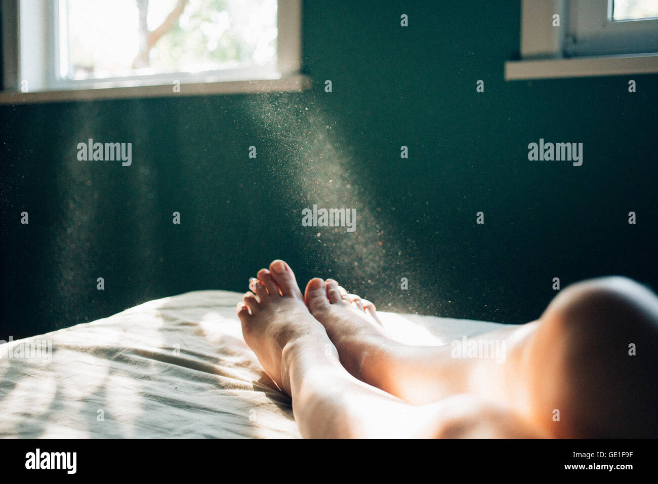 Sunlight streaming through window onto woman's legs on bed Stock Photo