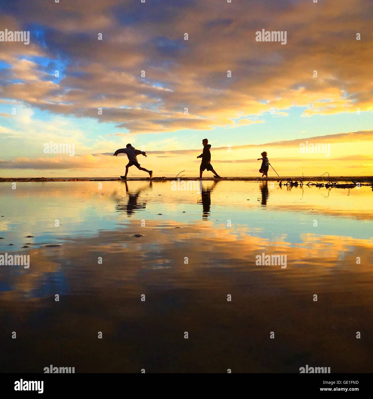 Three boys running along beach at sunset, Orange County, California, United States Stock Photo