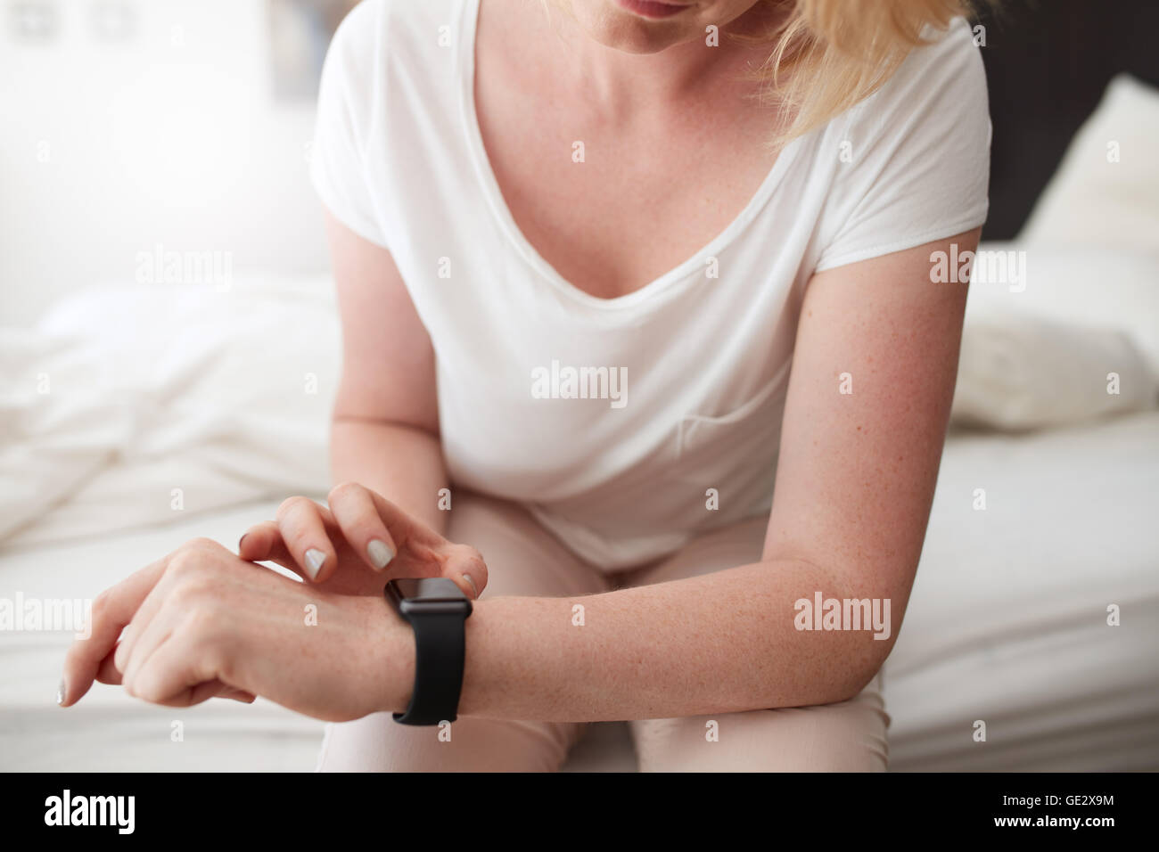Closeup shot of caucasian female checking time on her wrist watch while sitting on bed at home. Stock Photo