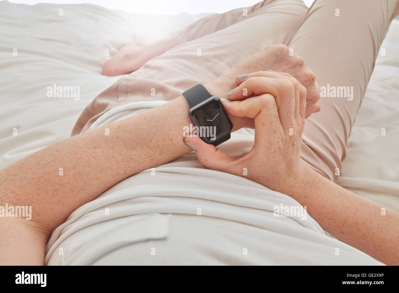 Close up image of woman using smartwatch to check time. Female lying on bed using smart wrist watch. Stock Photo