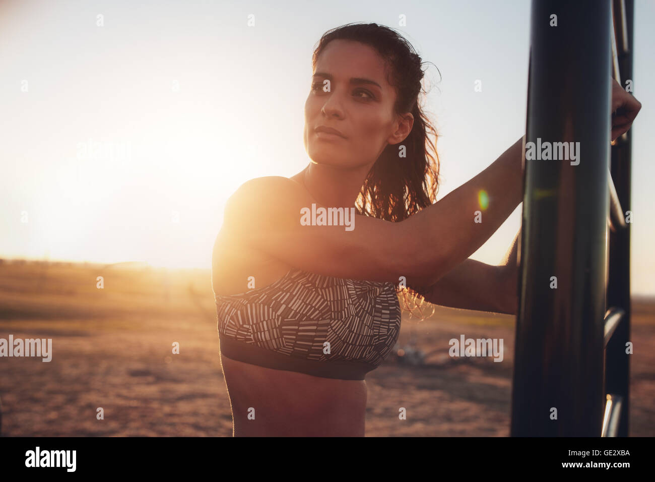 Portrait of fitness woman standing outdoors and looking away. Middle eastern female model in sportswear working out on wall bars Stock Photo