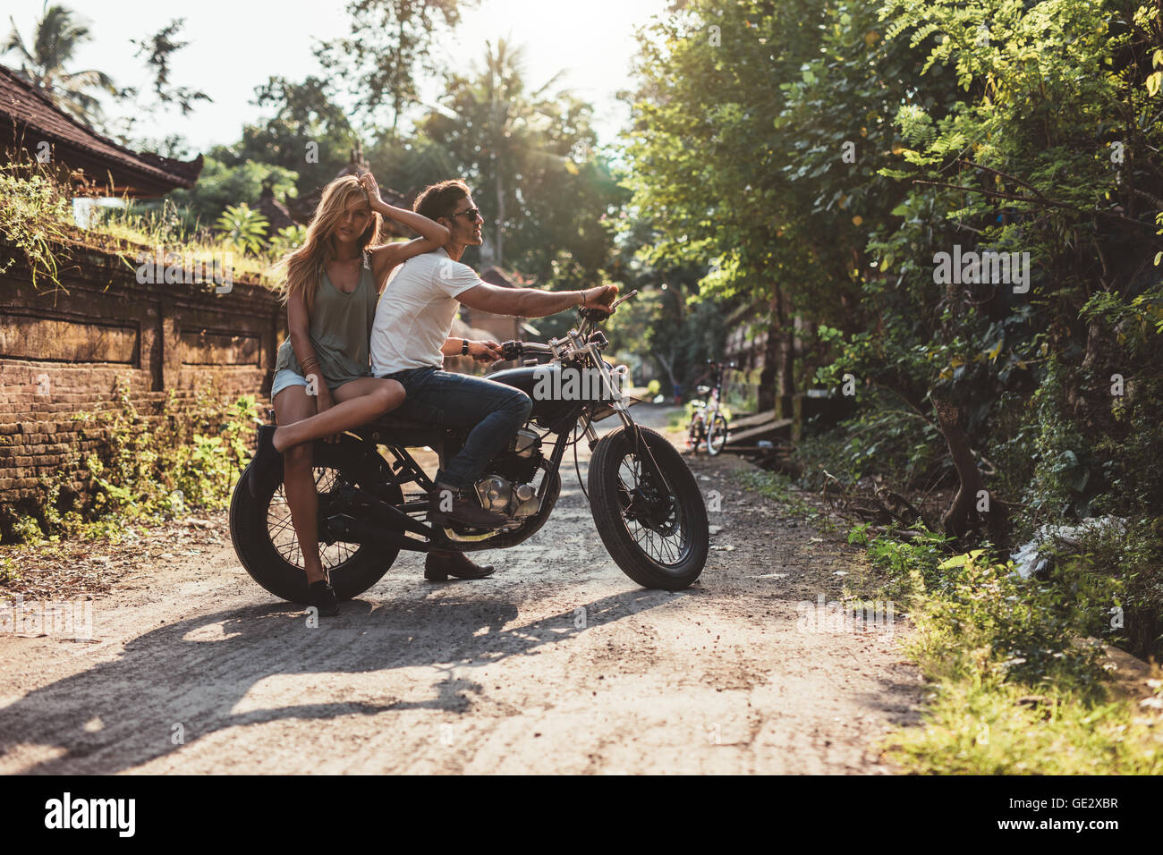 Portrait of young caucasian couple hanging out with motorcycle on village road. Young man and woman on motorbike. Stock Photo